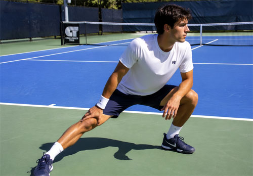Tennis player warming up with a stretch on court